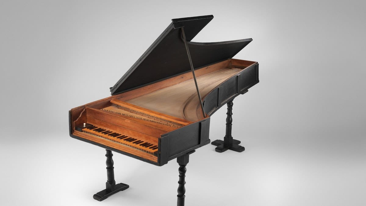 A black harpsichord with a wooden interior and turned legs on a white background