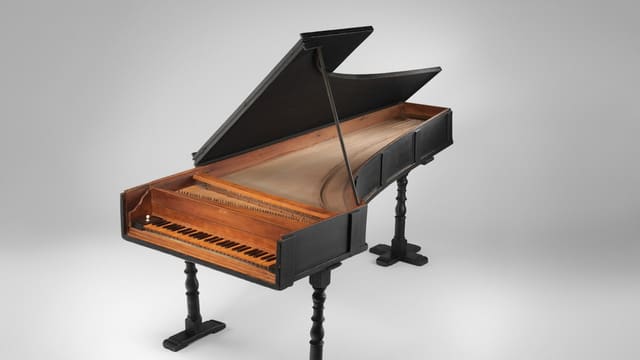 A black harpsichord with a wooden interior and turned legs on a white background
