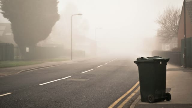 Un bac à ordures noir à roulettes posé en bordure de chaussée