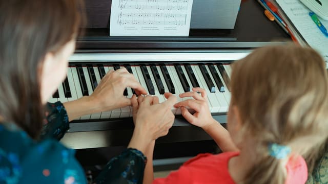 a woman and a little girl playing a piano