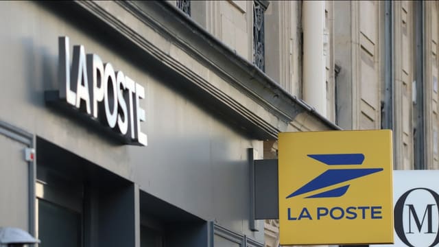 Enseigne jaune et bleue et lettres La Poste sur la façade en pierre d'un bureau de poste.