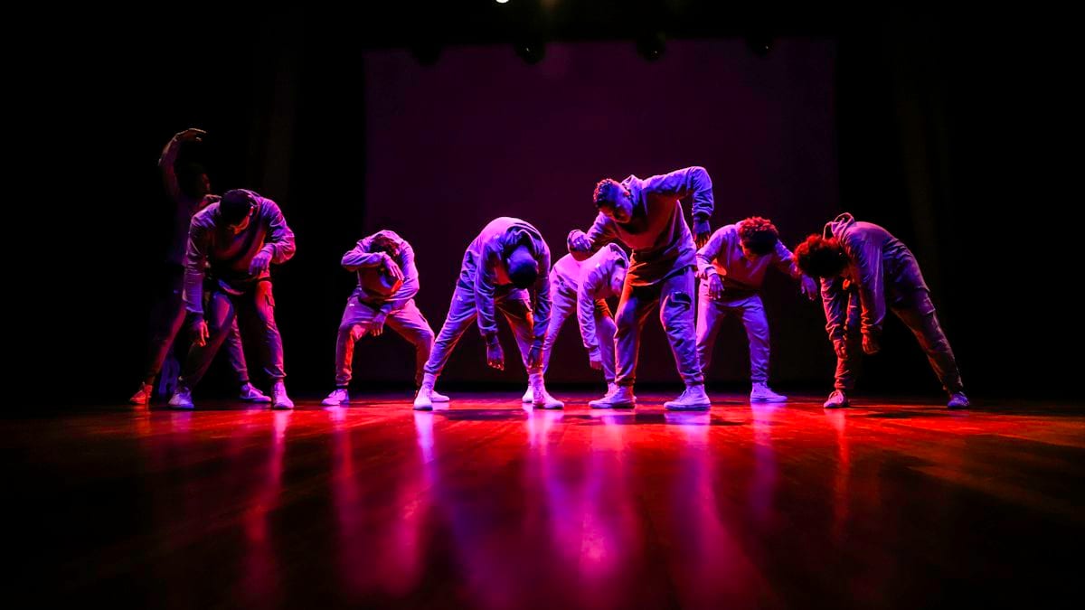 Groupe de danseurs hip-hop en mouvement sur une scène éclairée de violet et d'orange.