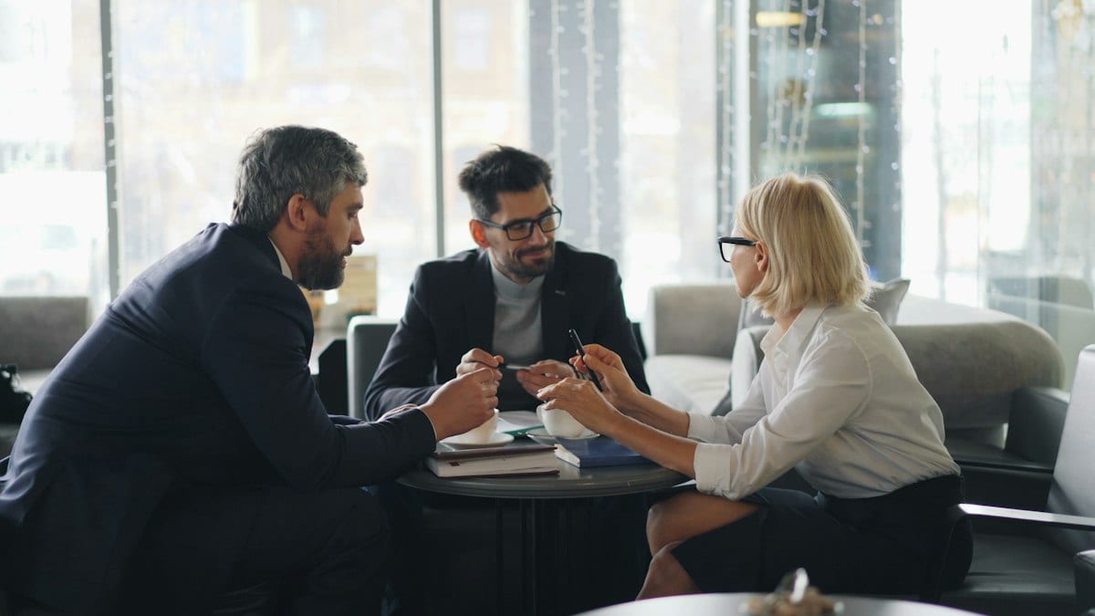 Trois professionnels échangent autour d'une table dans un café lors d'une rencontre d'affaires.