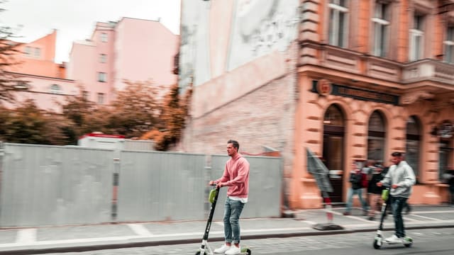 two men riding kick scooters during daytime