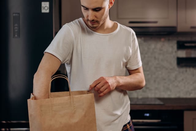 Male in white shirt unpacking groceries from paper bag in contemporary kitchen setting.