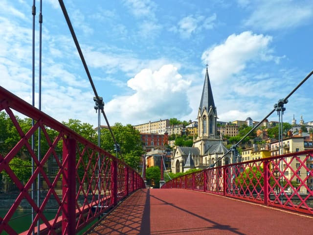 View of Saint George Church and Footbridge in Lyon, France under a blue sky.