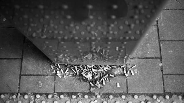 Cigarette butts litter the tiled ground near a structure.