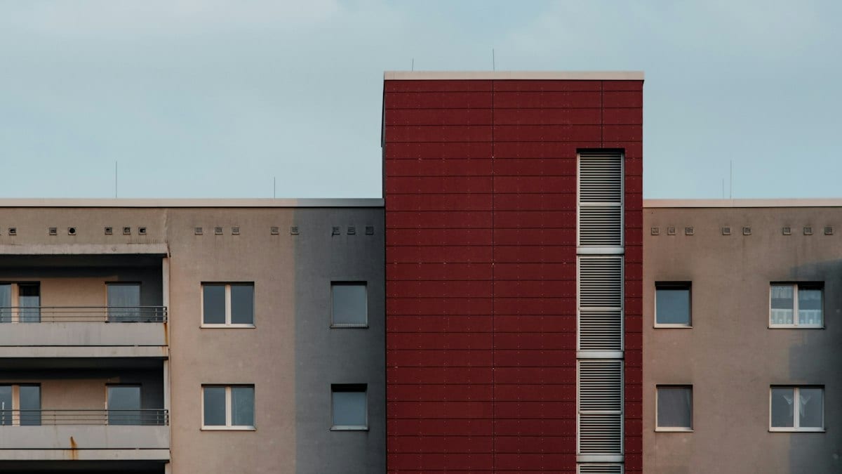 Façade d'un immeuble résidentiel aux teintes grises et rouges, illustrant un habitat collectif récent.