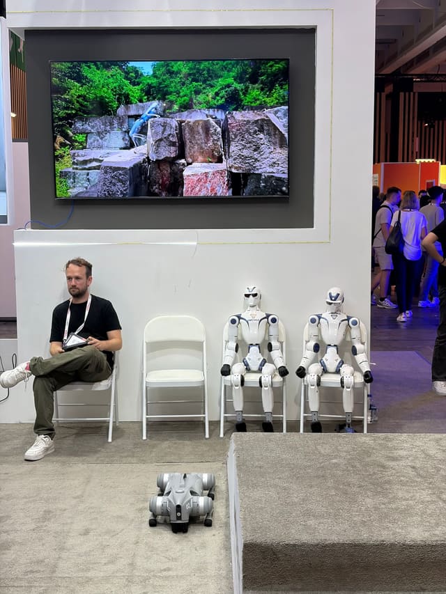 Deux robots humanoïdes assis sur des chaises à côté d'un visiteur, à VivaTech 2026